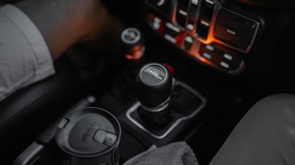 Detailed view of a Jeep's manual gear shift in a dimly lit cabin with cup holder.