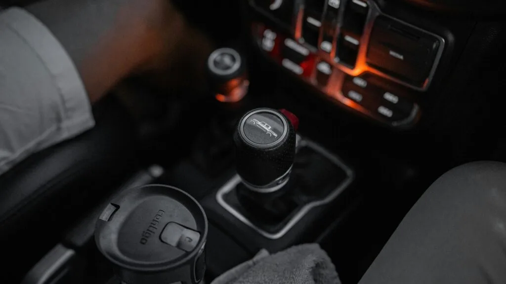 Detailed view of a Jeep's manual gear shift in a dimly lit cabin with cup holder.